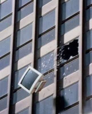 a vintage computer monitor is seen falling from a broken window on a tall building, with glass shards flying outward. The…