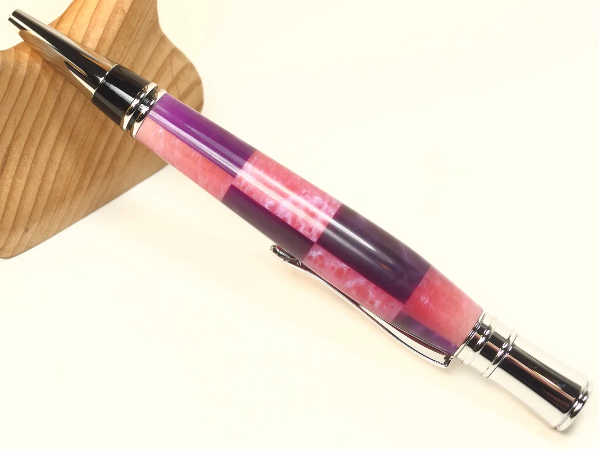 A close-up photo of a decorative pen with alternating pink and purple translucent sections and silver metal accents, resting…