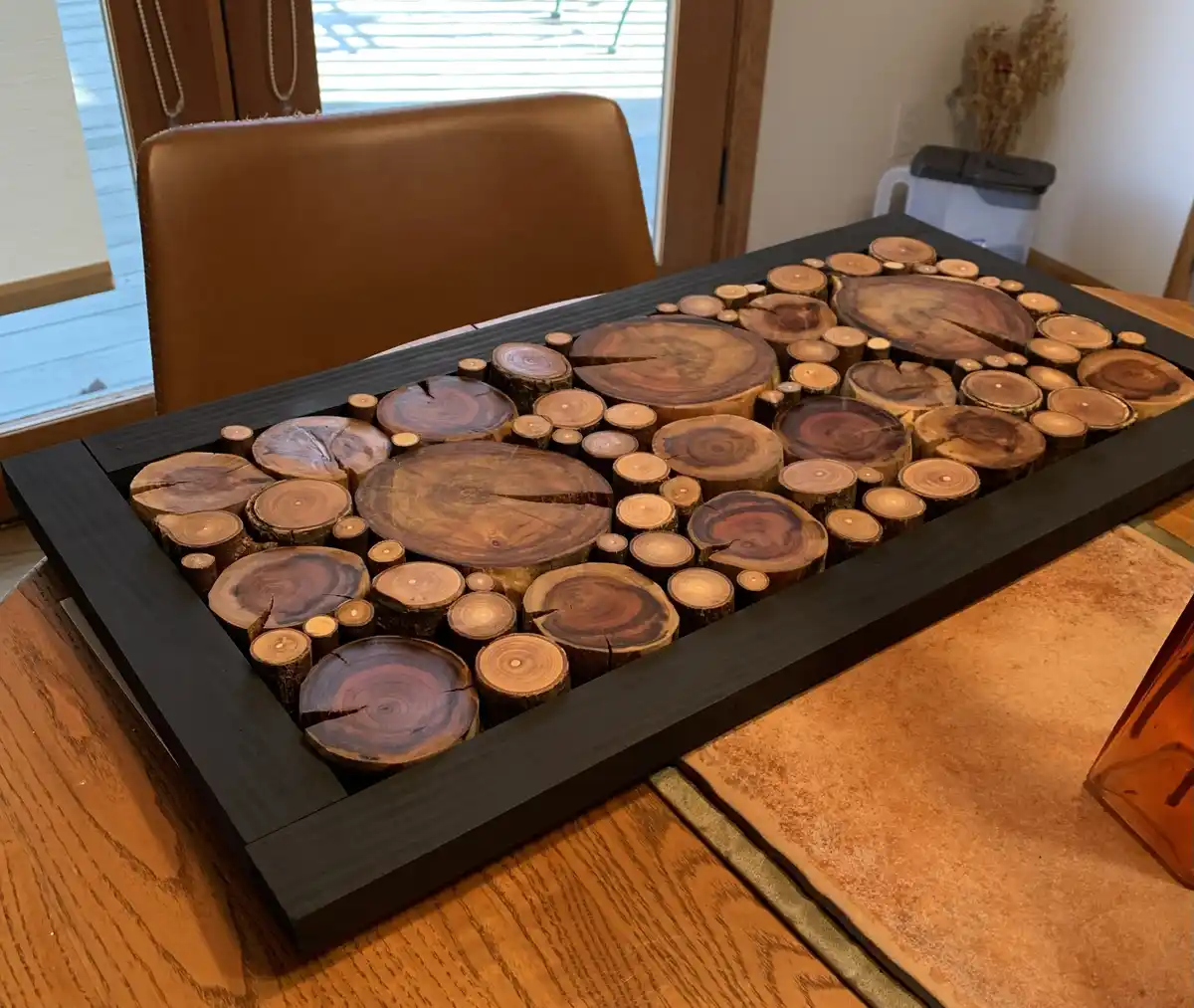 A rectangular black-framed decorative piece made of numerous circular wood slices of varying sizes and grain patterns…