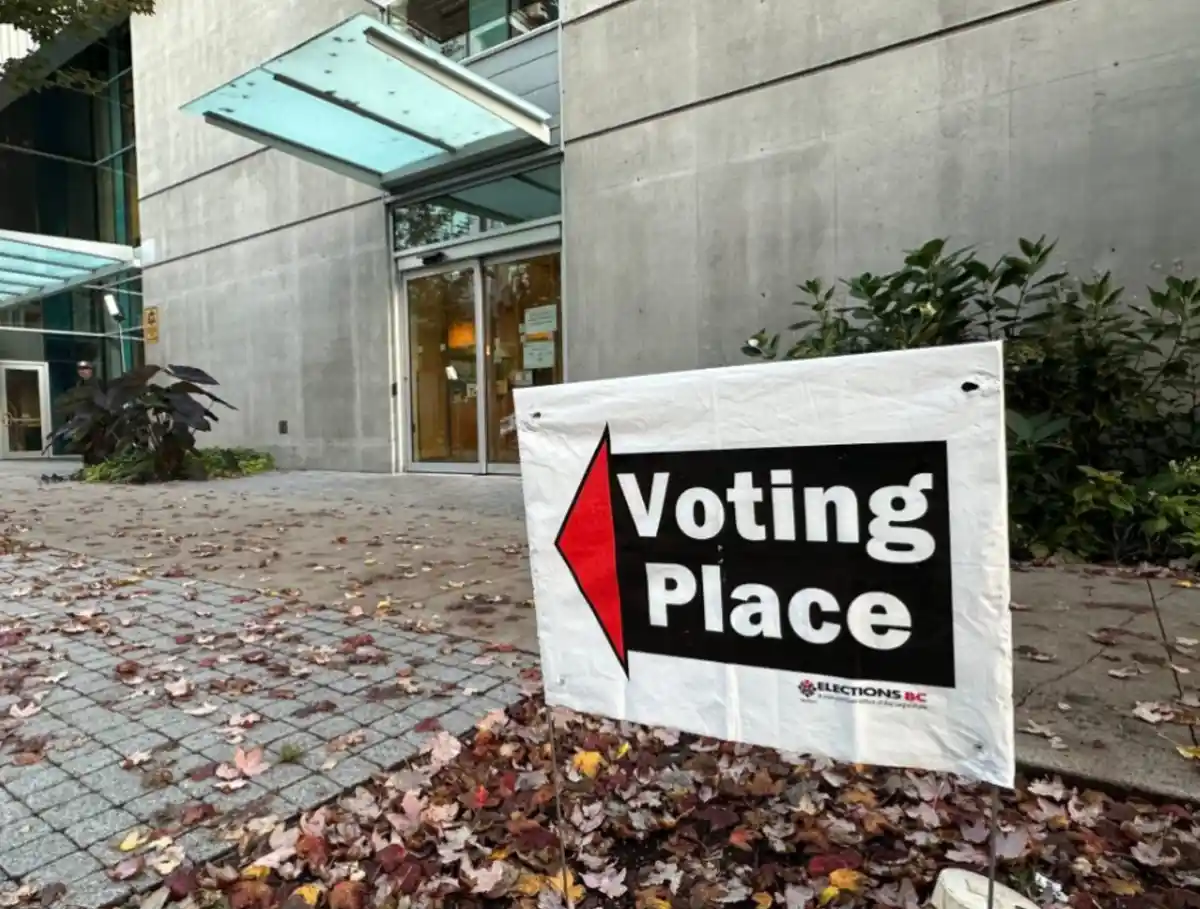 A white directional sign with a red arrow pointing left and the words 'Voting Place' in bold white text on a black…