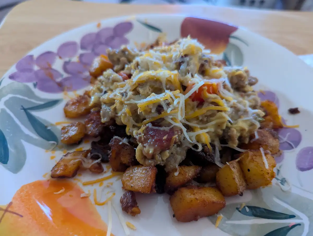 A close-up photo of a plate of breakfast food, featuring crispy hash browns, scrambled eggs, crumbled bacon, and shredded…