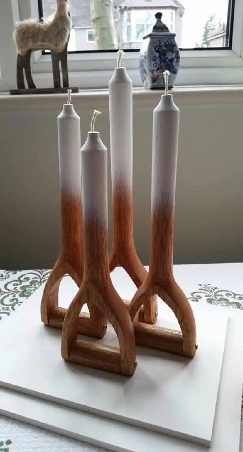 Four white candles with wooden spoon bases are arranged on a white surface near a window. The candles have a gradient from…