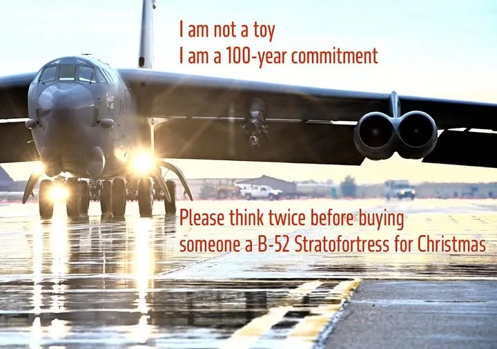 A large military B-52 Stratofortress bomber is pictured on a wet tarmac with its landing lights on, reflecting in the water…
