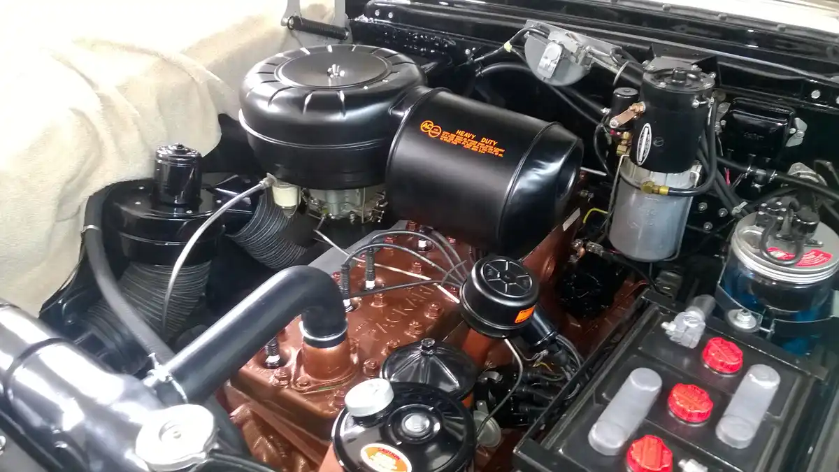 A close-up photo of a meticulously maintained classic car engine bay, featuring a shiny copper-colored engine block, black…