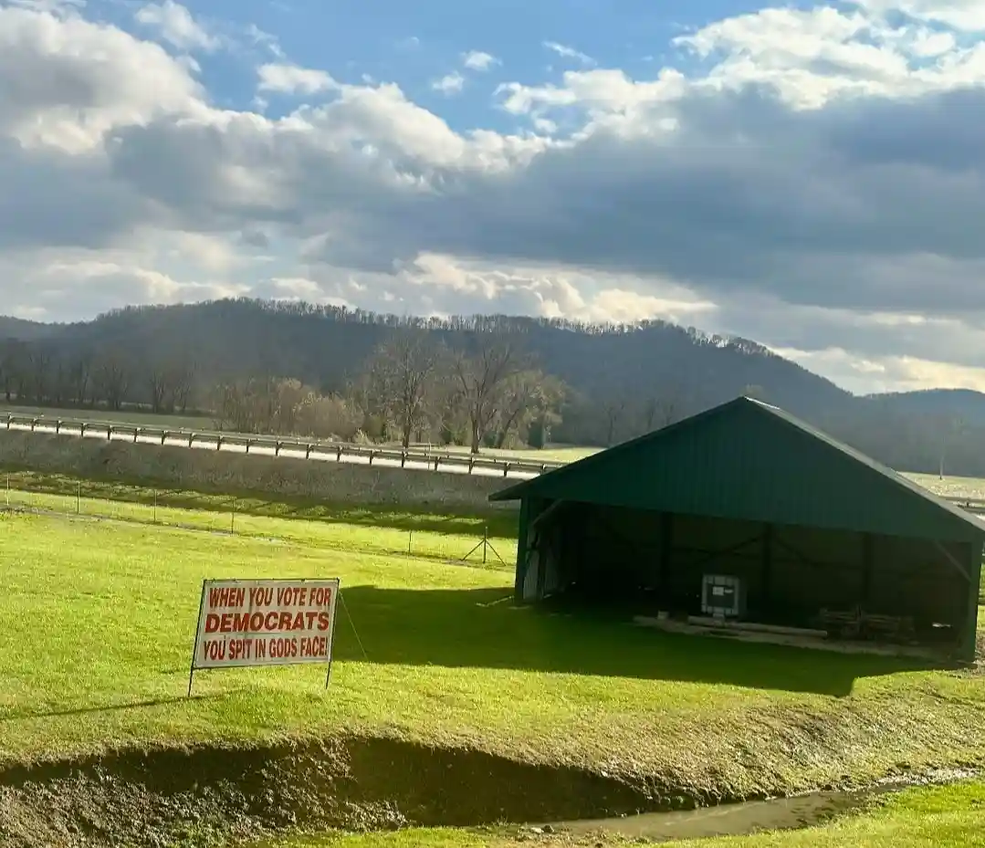 A rural landscape with a green barn, rolling hills, and a cloudy sky, featuring a white sign with red text that reads 'WHEN…