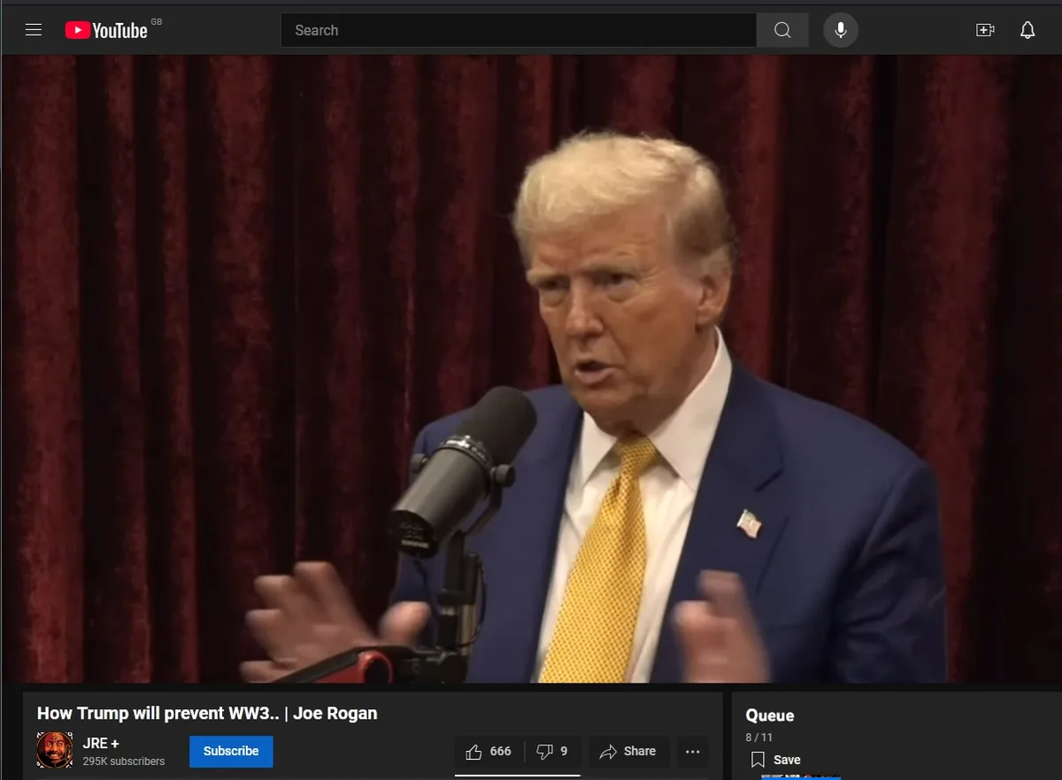 A screenshot from a YouTube video shows Donald Trump speaking into a microphone while gesturing with both hands. He is…