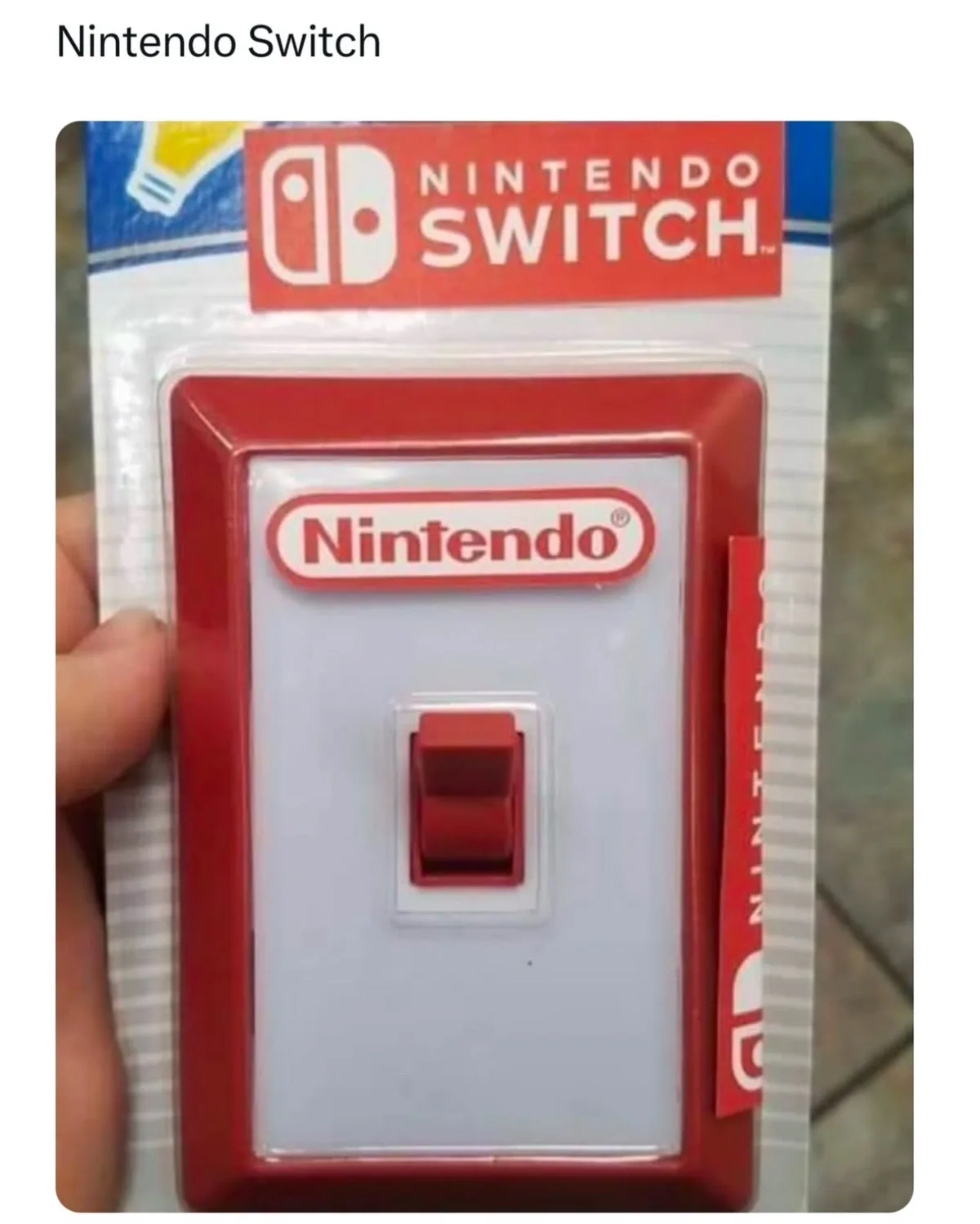 A hand holds a Nintendo Switch retail box, but the front panel has been replaced with a red light switch, complete with the…
