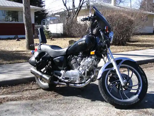 A black Yamaha motorcycle with chrome accents is parked on a residential street next to a curb, with houses and bare trees…