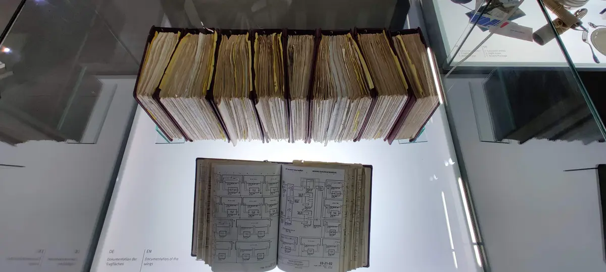 A museum display shows an open manual labeled 'Concorde WIRING DIAGRAM MANUAL' with technical schematics, positioned below a…