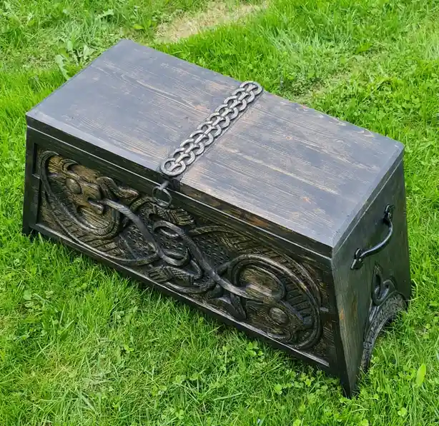 A dark wooden treasure chest with ornate carvings and a metal chain strap sits on green grass. The overlaid text reads 'my…