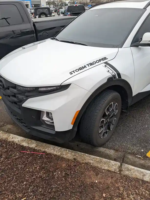 A white SUV is parked in a lot with the words 'STORM TROOPER' written in black lettering along its hood. The vehicle has…