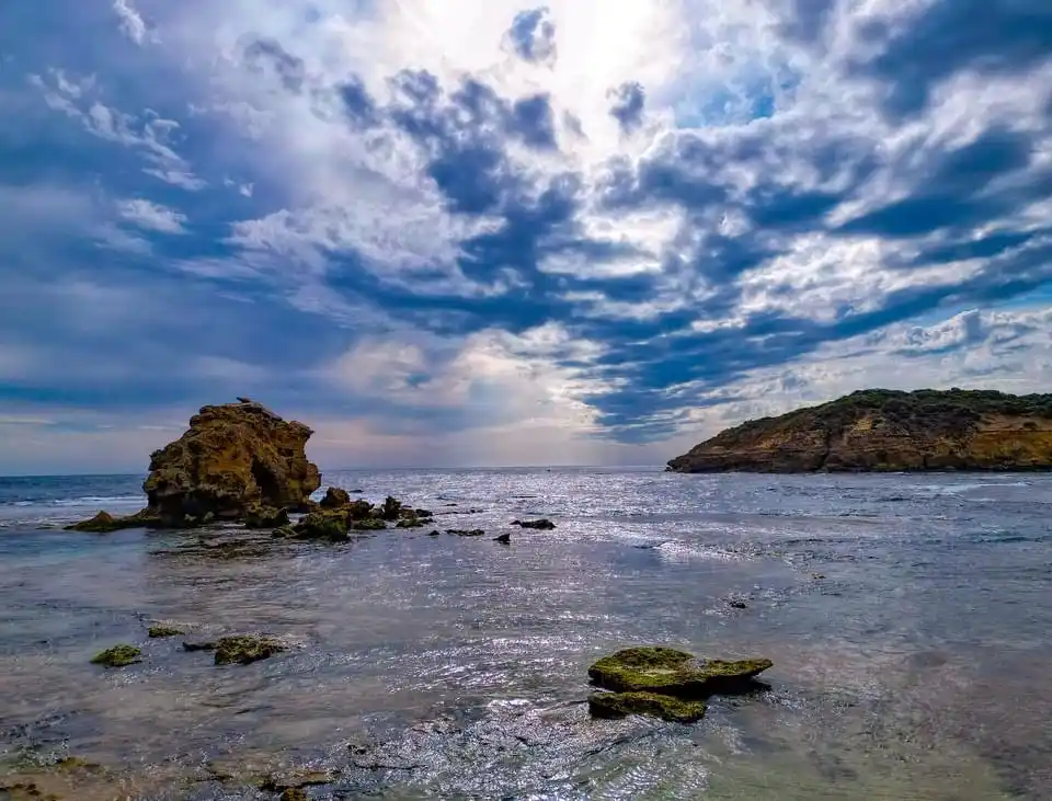 A scenic coastal photo shows a calm sea with scattered rocks and a dramatic, cloudy sky. Overlaid text reads 'i'm not lazy…
