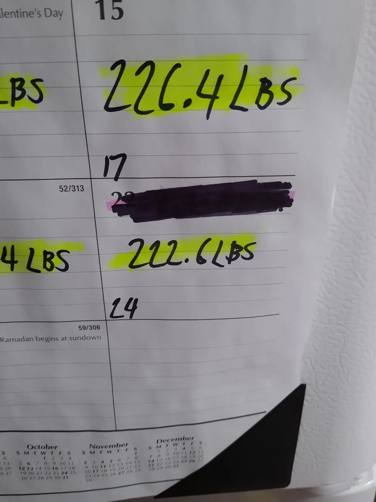 A close-up of a handwritten weight tracking calendar showing a weight loss journey, with entries like '226.4 LBS' and '222.6…