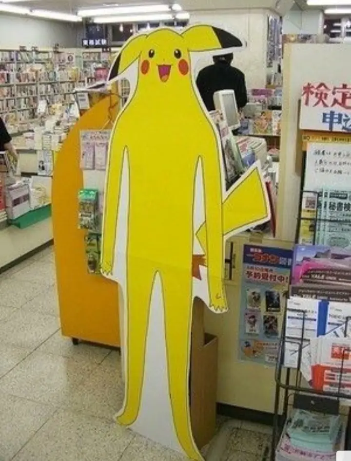 A tall, yellow cardboard cutout of the Pokémon Pikachu stands in a Japanese bookstore aisle, its head and upper body visible…