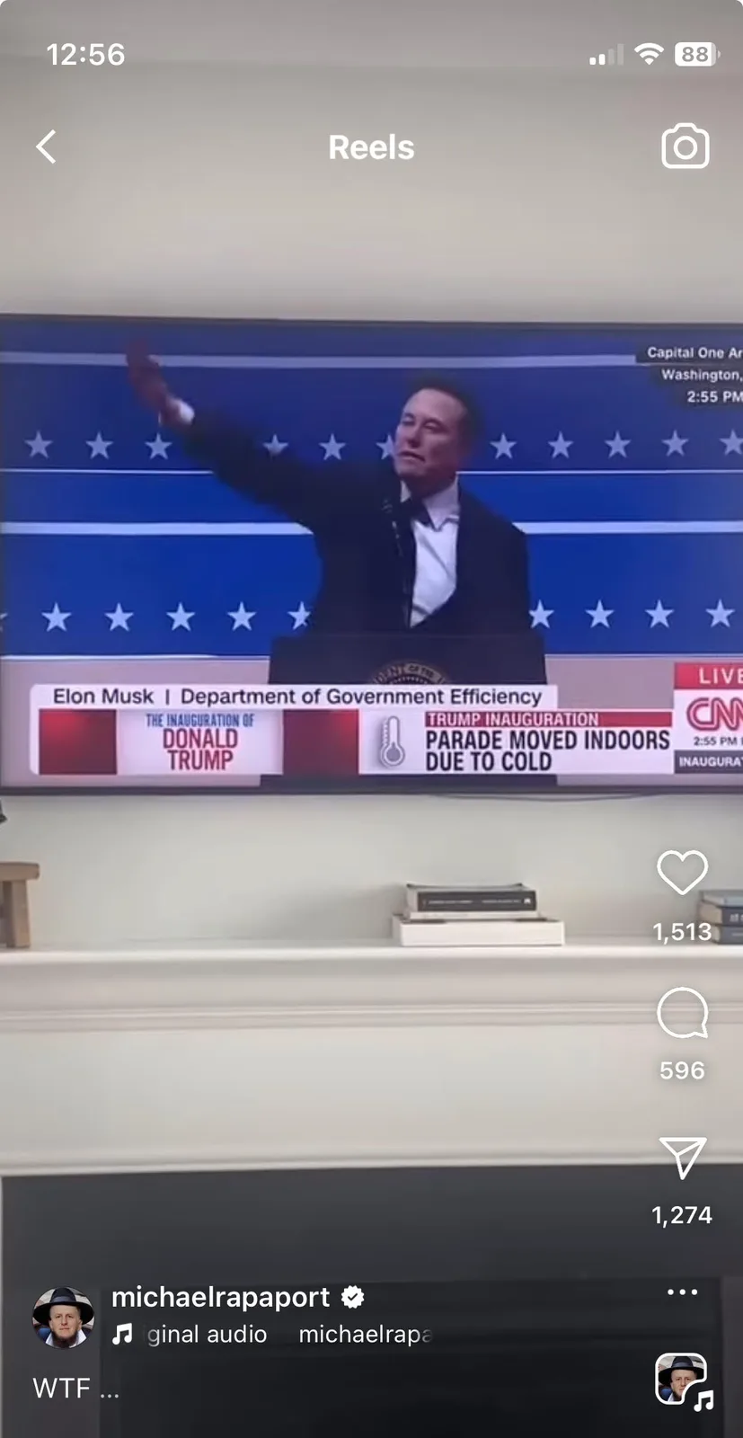 A television screen shows a man in a suit, identified as Elon Musk, speaking at a podium with a blue star-spangled backdrop…
