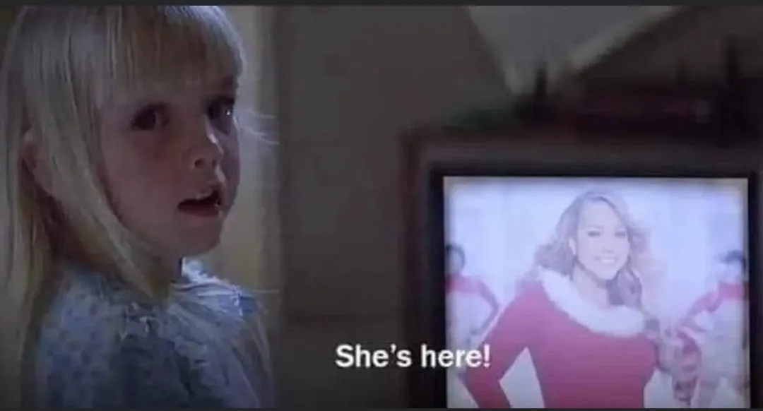 A young blonde girl with wide eyes and an open mouth stares in shock at a television screen showing a smiling woman in a red…