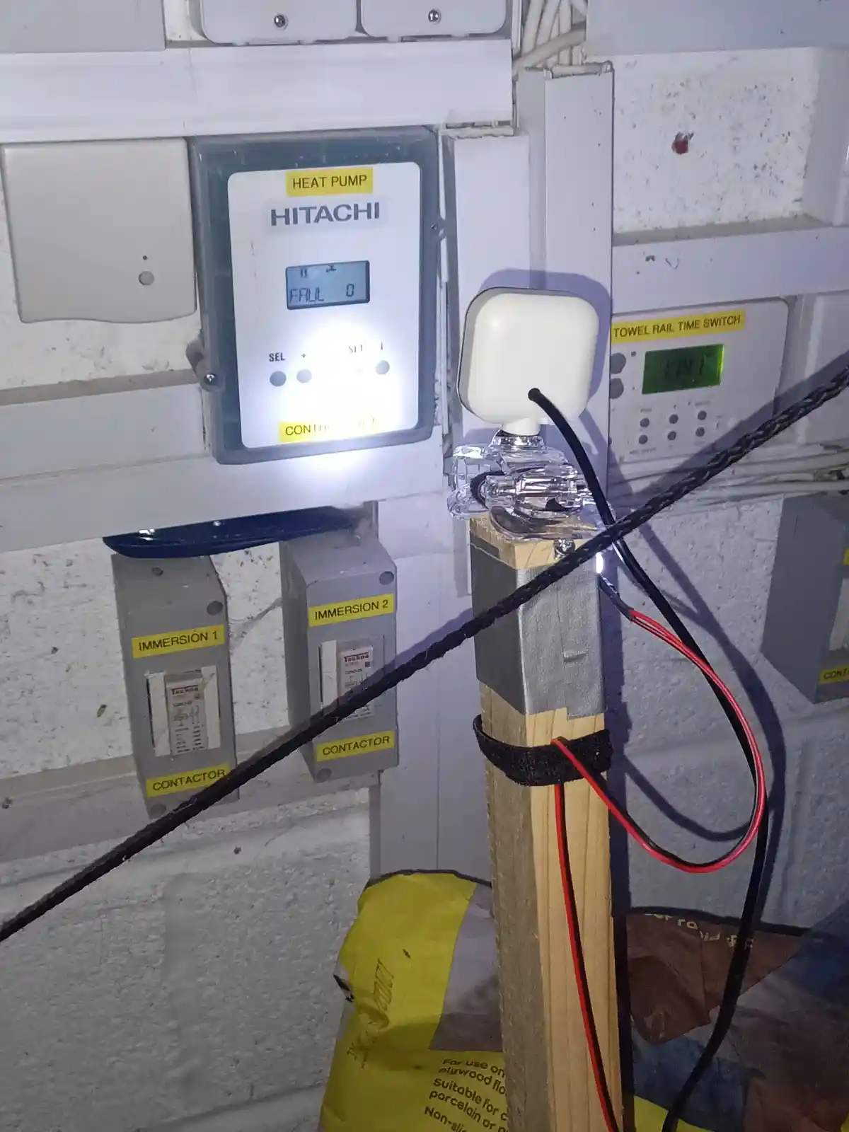 A Hitachi heat pump control panel displays 'FRUL 0' on its screen, next to a towel rail time switch and immersion heaters. A…