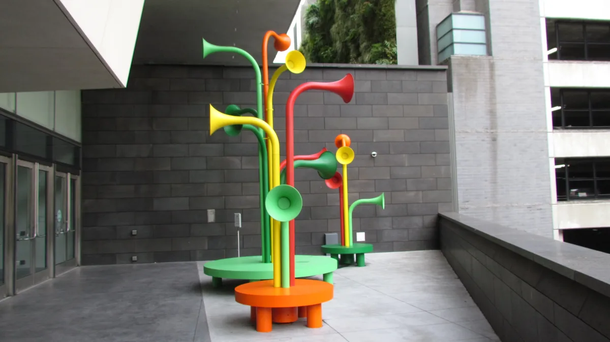 The image shows two brightly colored, abstract sculptures resembling musical instruments or flowers, standing on circular…
