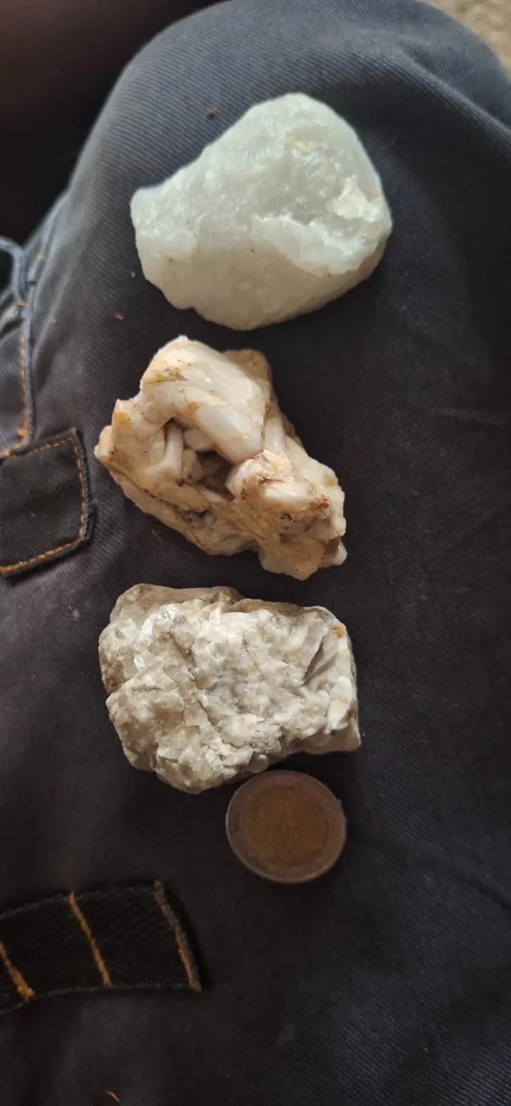 Three irregularly shaped, light-colored rocks of varying textures are arranged vertically on a dark denim surface, with a…