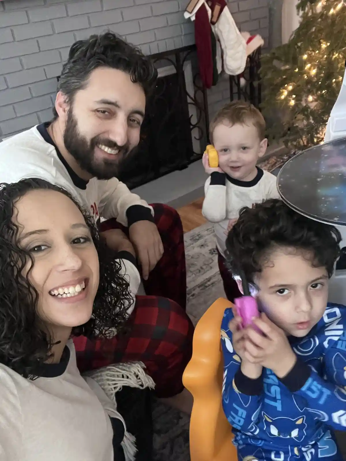 A family photo shows a smiling man and woman in pajamas with two young children. One child holds a yellow toy phone to their…