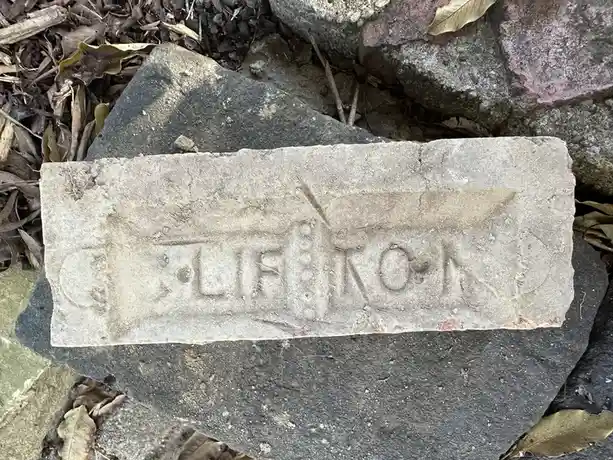 A weathered, rectangular concrete brick with the word 'tufa' embossed on its surface lies among rocks and dry leaves. The…