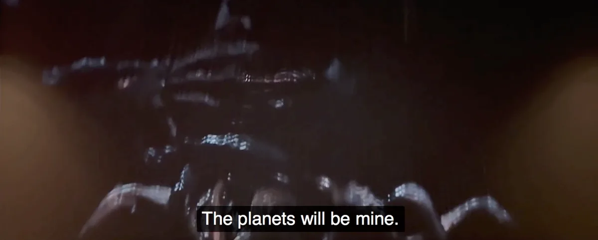 A dark, blurry, low-resolution image shows a menacing, multi-limbed alien creature looming in a dimly lit environment, with…