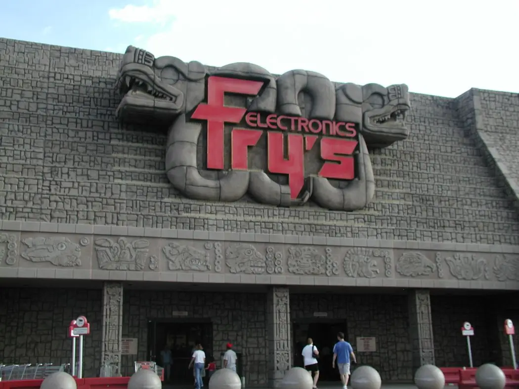 The exterior of a Fry's Electronics store features a large, red, stylized logo of 'Fry's Electronics' set within a gray…