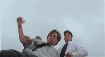A sequence of six frames from a movie scene shows four men in business attire struggling to carry a fifth man through a…