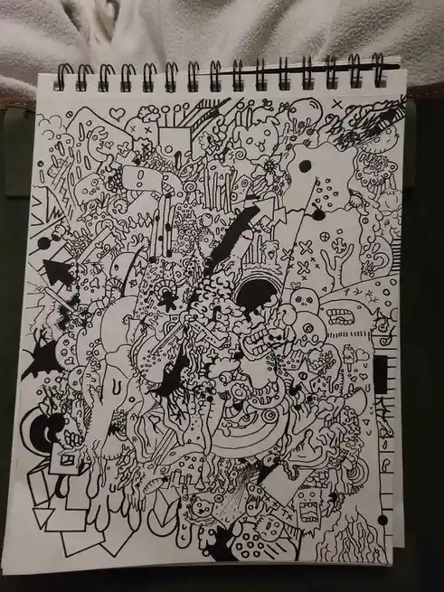A black-and-white ink drawing on a spiral-bound notebook page, filled with chaotic, overlapping doodles including skulls…