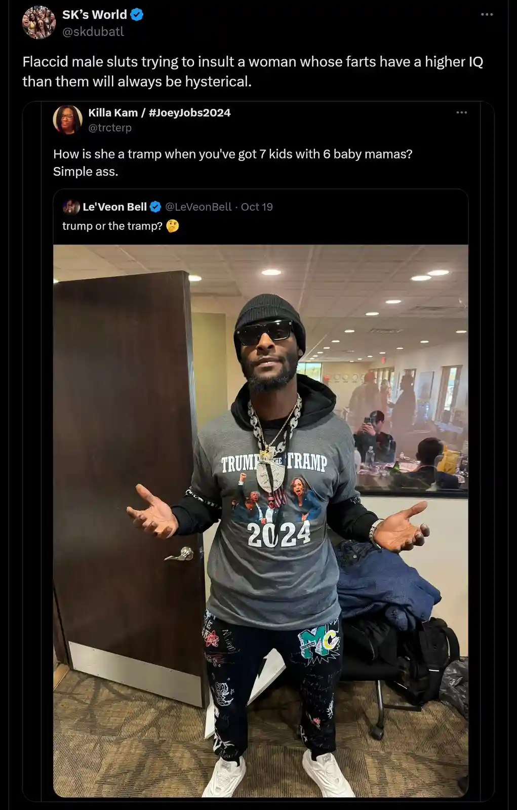 A man wearing a 'TRUMP THE TRAMP 2024' t-shirt and a beanie stands with his hands open in a room, reacting to a Twitter…