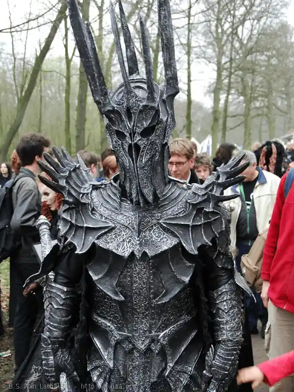 A person in an elaborate, menacing black costume resembling a fantasy villain with a spiked helmet and armor stands in a…