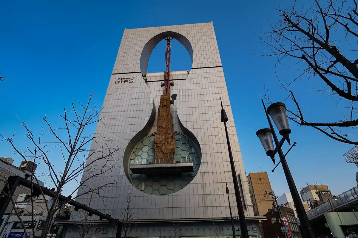 A low-angle photo shows the Namba HIPS building in Osaka, Japan, featuring its iconic large circular cutout and a rock…