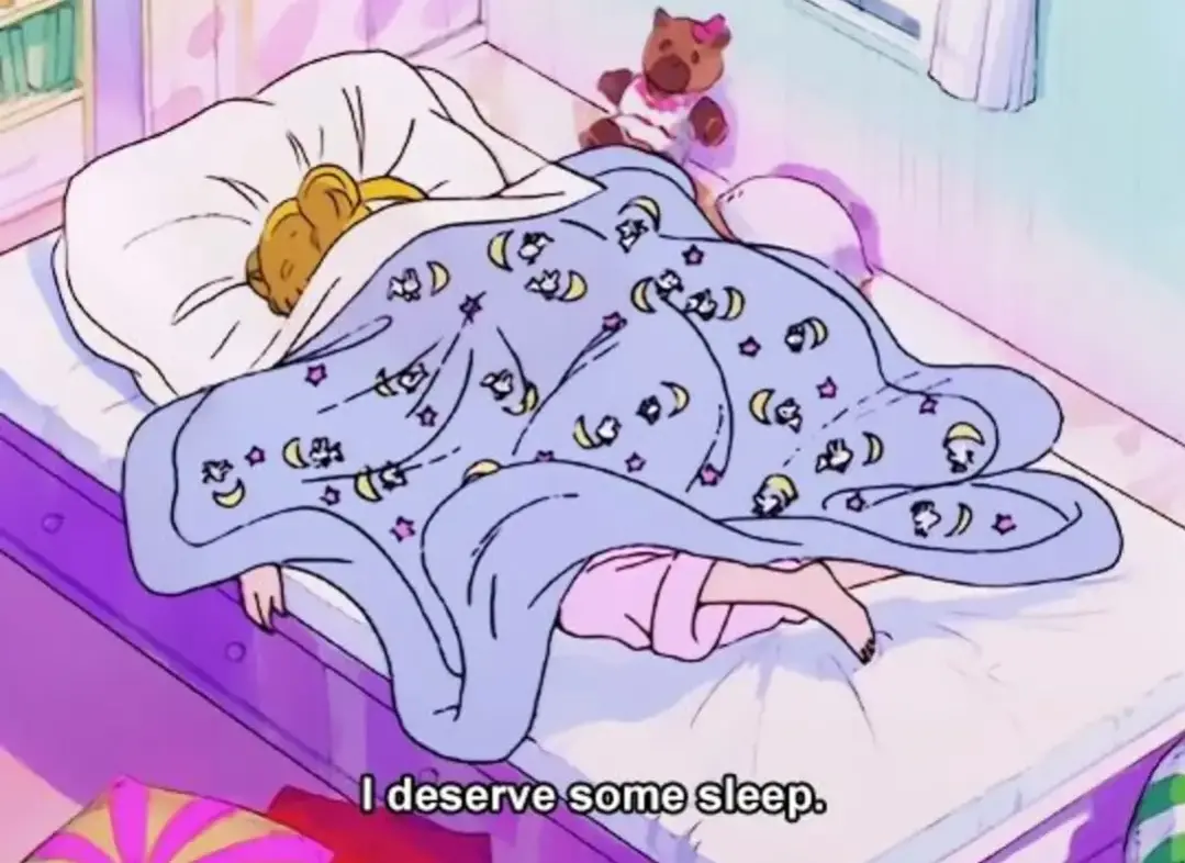 An anime-style girl with blonde hair is sleeping in bed under a blue blanket with moon and star patterns, her feet sticking…