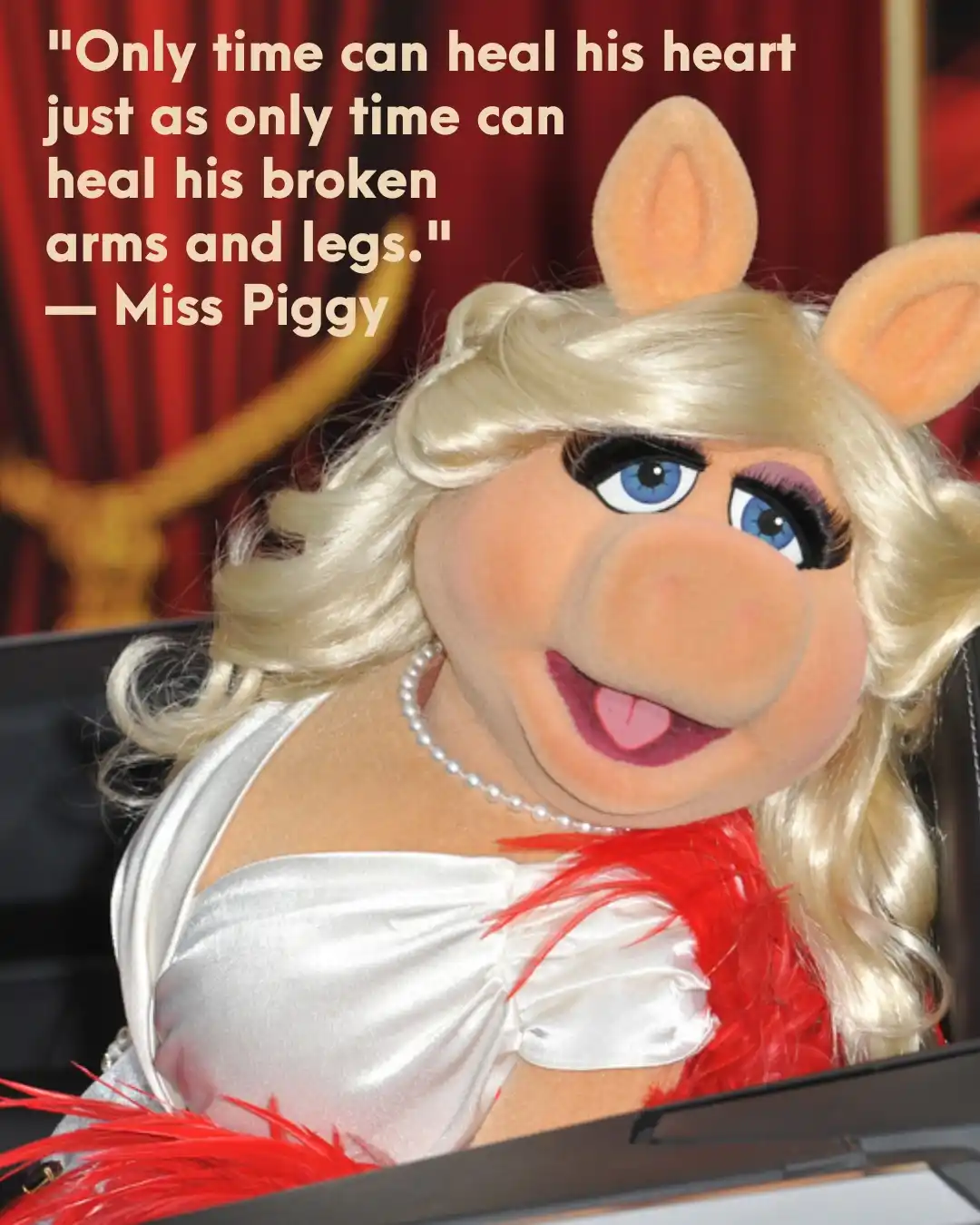 A close-up photo of the Muppet character Miss Piggy, who has blonde hair, blue eyes, and is wearing a white satin top with…