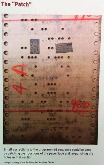 A close-up of an old, worn paper tape with holes, showing a section where a rectangular patch has been applied over some…