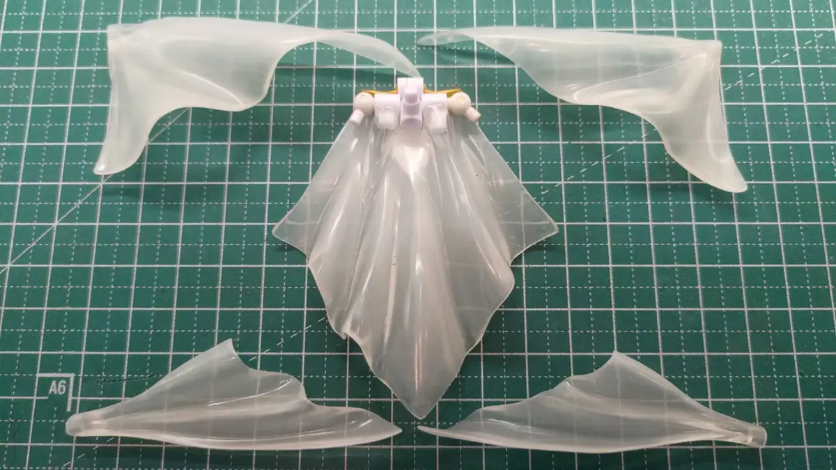 A photo shows four translucent plastic pieces arranged on a green cutting mat, resembling bat wings. The central piece is…