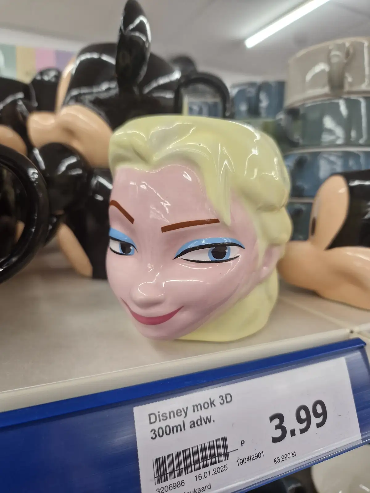 A close-up of a ceramic mug shaped like Elsa from Disney's Frozen, displayed on a store shelf with a price tag reading…