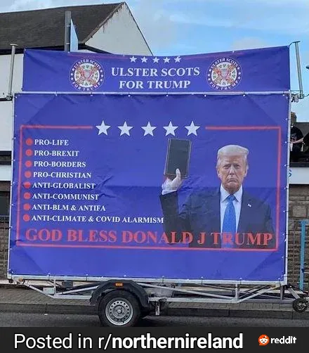 A large blue political banner on a trailer displays a photo of Donald Trump holding a book, with the text 'ULSTER SCOTS FOR…