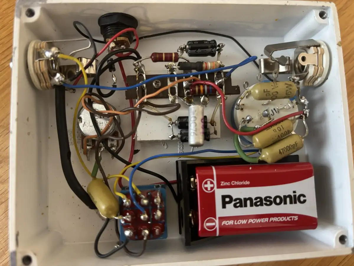 A close-up photo of a white electronic device's interior, showing a messy tangle of wires, resistors, capacitors, and a…