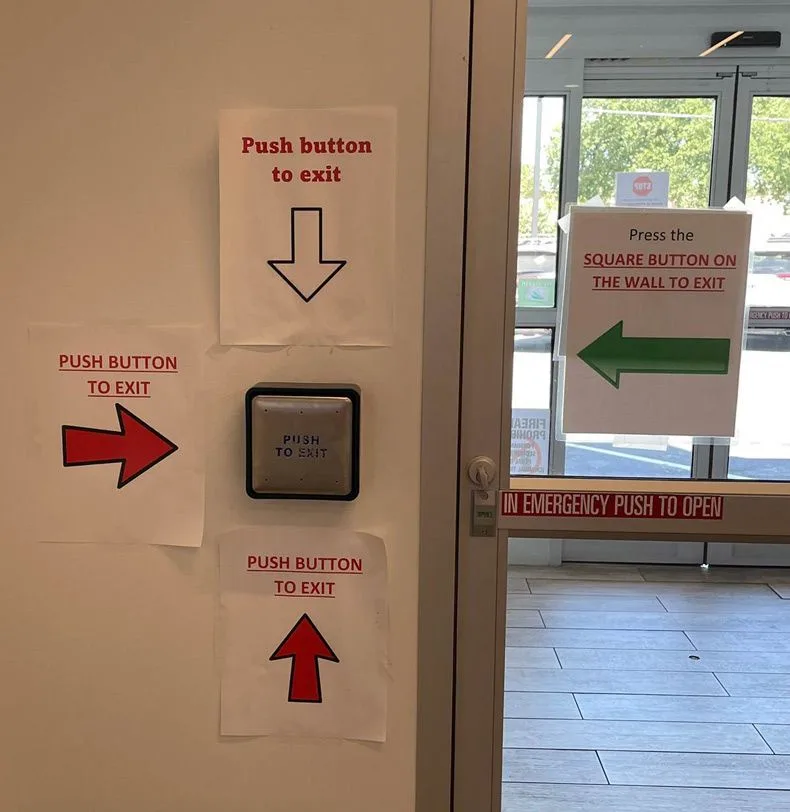 A wall has multiple signs with arrows pointing in different directions (up, down, left, right) all telling people to 'push…