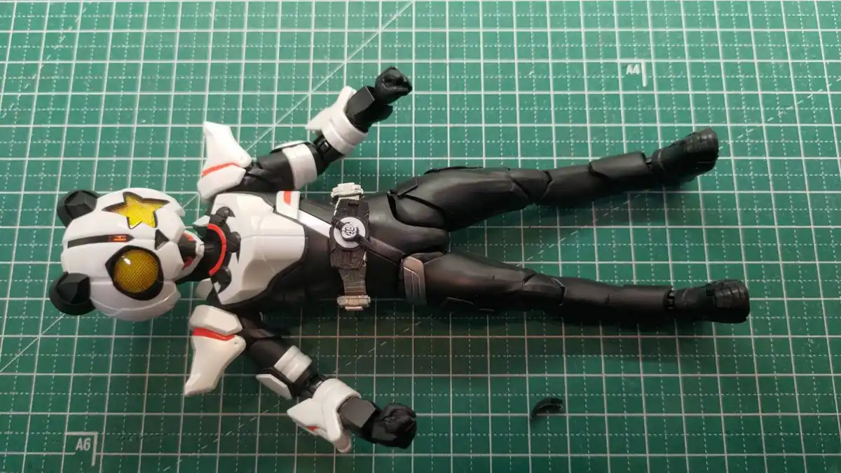 A black-and-white action figure with a panda-themed helmet featuring a yellow star and large yellow eye, lies flat on its…