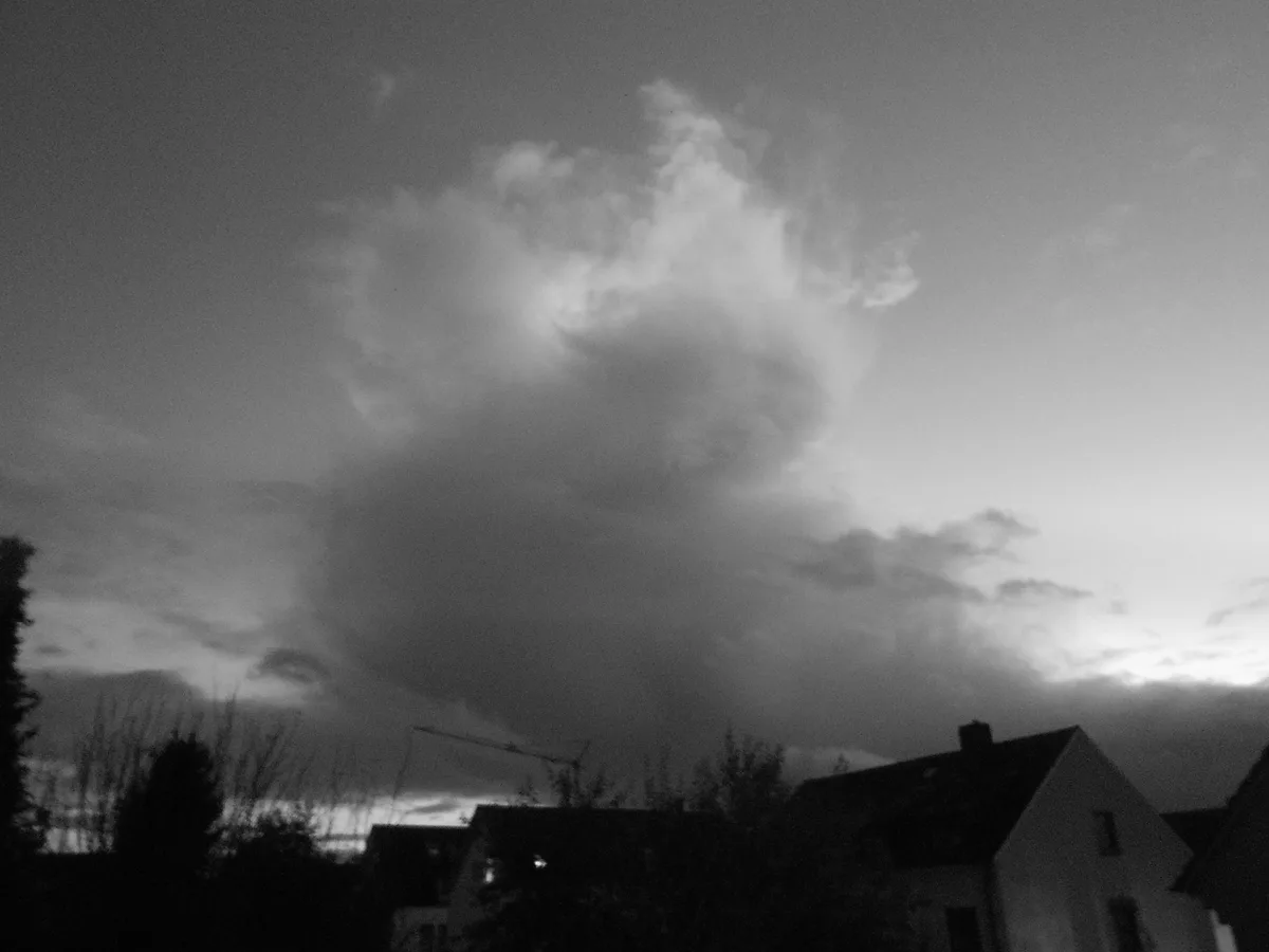A black-and-white photo shows a large, dramatic cloud formation in the sky that resembles a human face with a frowning…