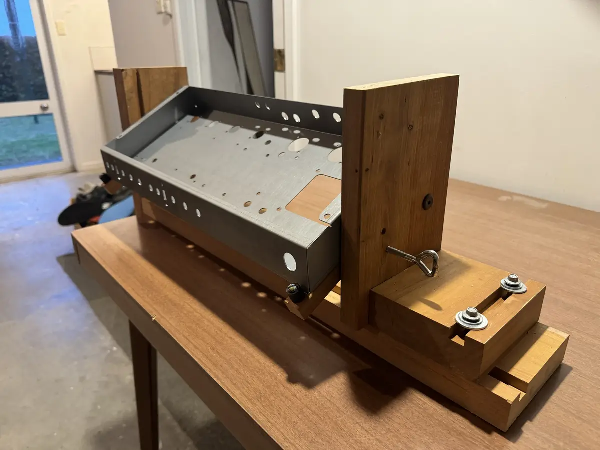 A homemade grill constructed from a metal box with holes and wooden supports, mounted on a wooden table. The metal box has a…