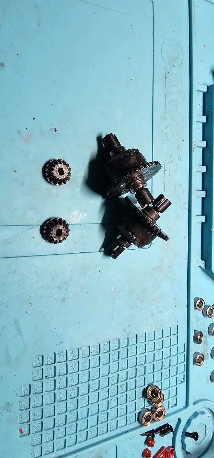 A close-up photo shows disassembled car transmission gears and components resting on a light blue plastic tool tray with…