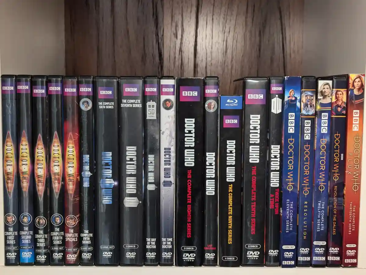 A row of Doctor Who DVD and Blu-ray cases from various series, including First through Thirteenth, are neatly arranged on a…