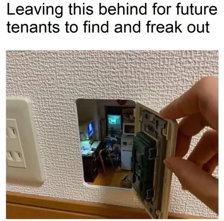 A hand pulls open a wall plate, revealing a hidden camera lens pointed into a cluttered room with a TV and desk. The…