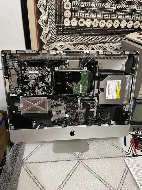 An Apple iMac with its back panel removed, exposing its internal components including circuit boards, a hard drive, and…
