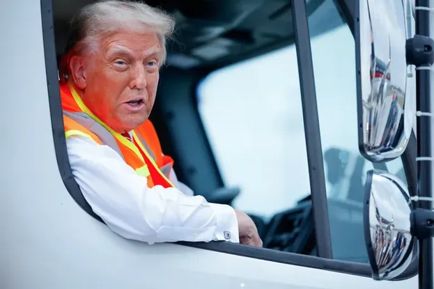 a man with white hair wearing an orange safety vest and white shirt leans out of the driver's side window of a white truck…
