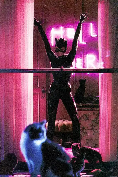 A person in a black, shiny Catwoman costume stands on a bar with arms raised triumphantly in front of a pink neon sign that…