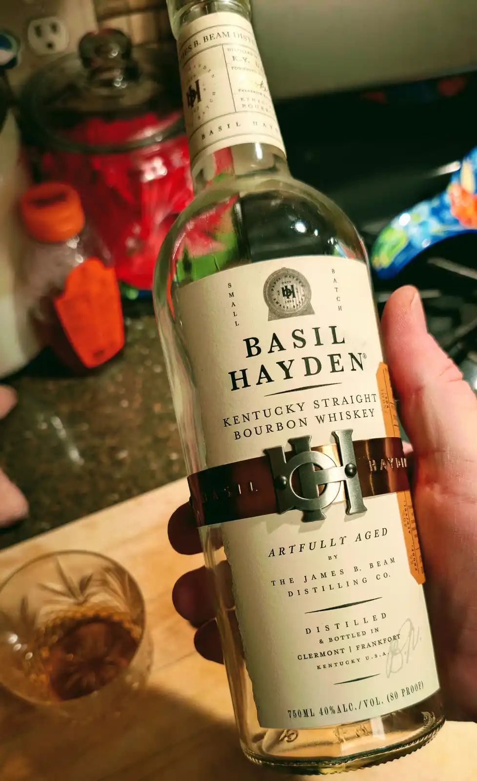 A hand holds a bottle of Basil Hayden's Kentucky Straight Bourbon Whiskey, with the brand name clearly visible on the label…
